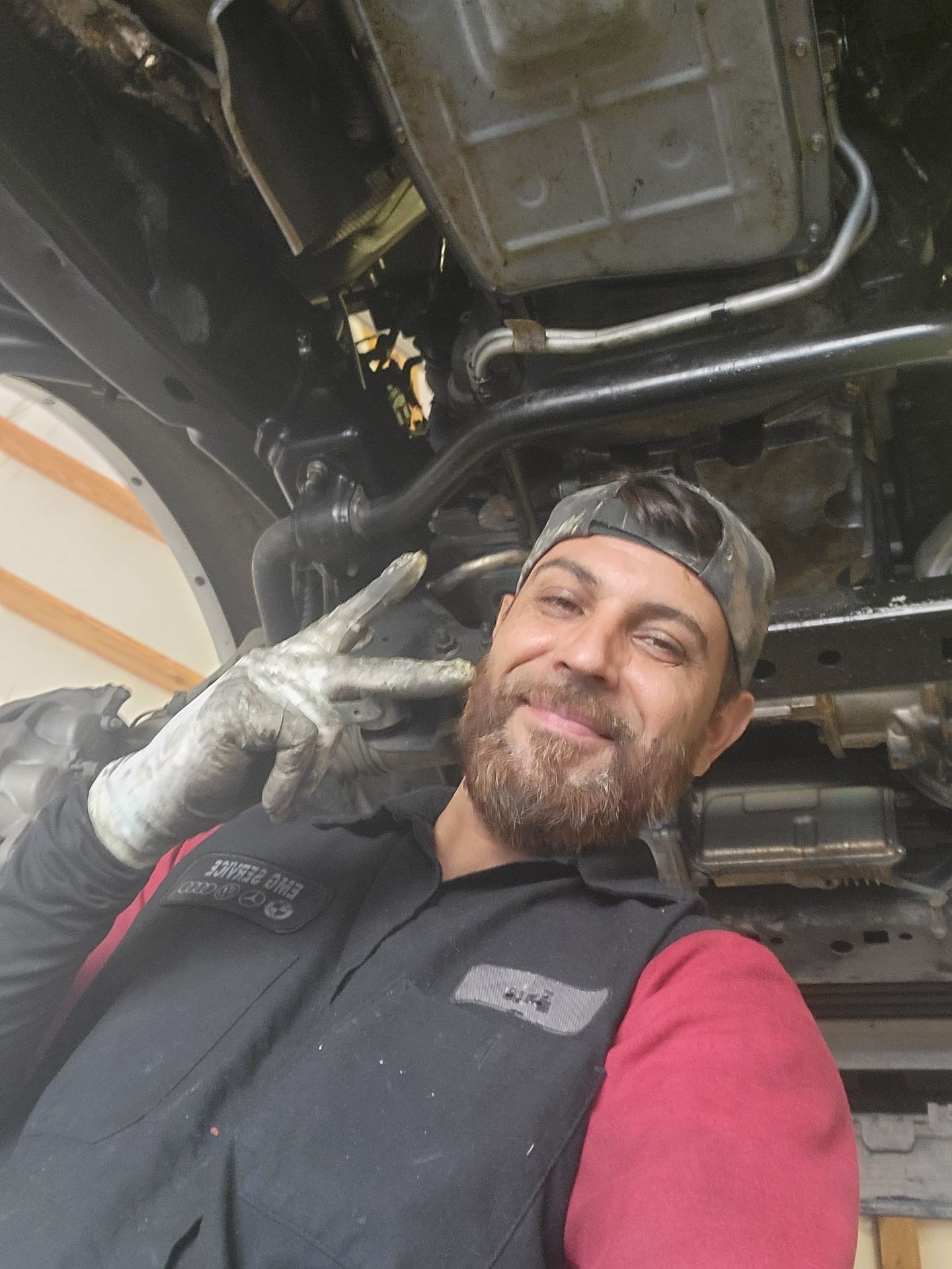 Mechanic in uniform showing peace sign while working under a vehicle.